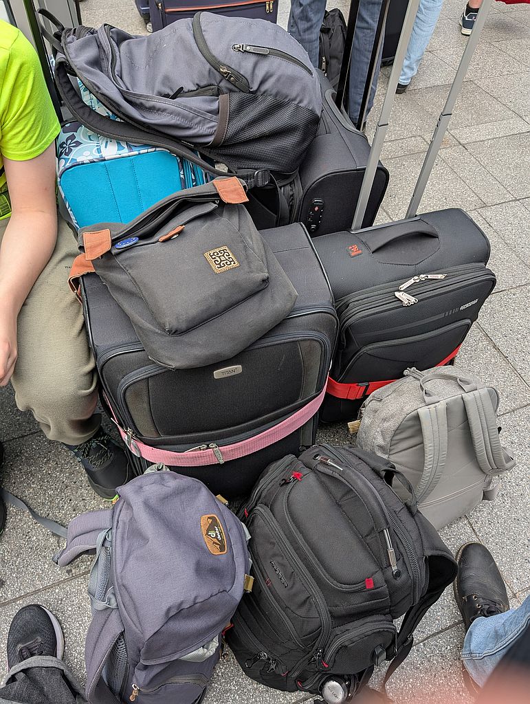 Vier Koffer, vier Rucksäcke und eine Handtasche zusammengestellt und gestapelt neben der Wartebank auf einem Bahnhof.