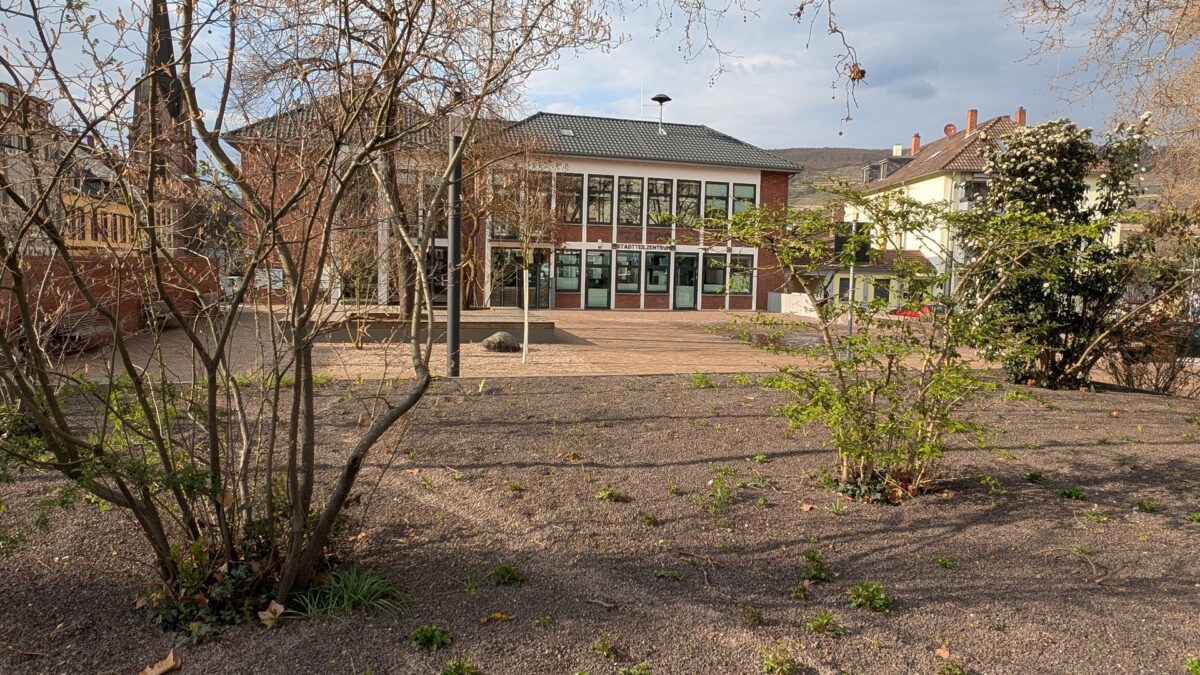 Der rötlich gepflasterte neue Platz vor dem Stadtteilzentrum, umrahmt von Bäumen.